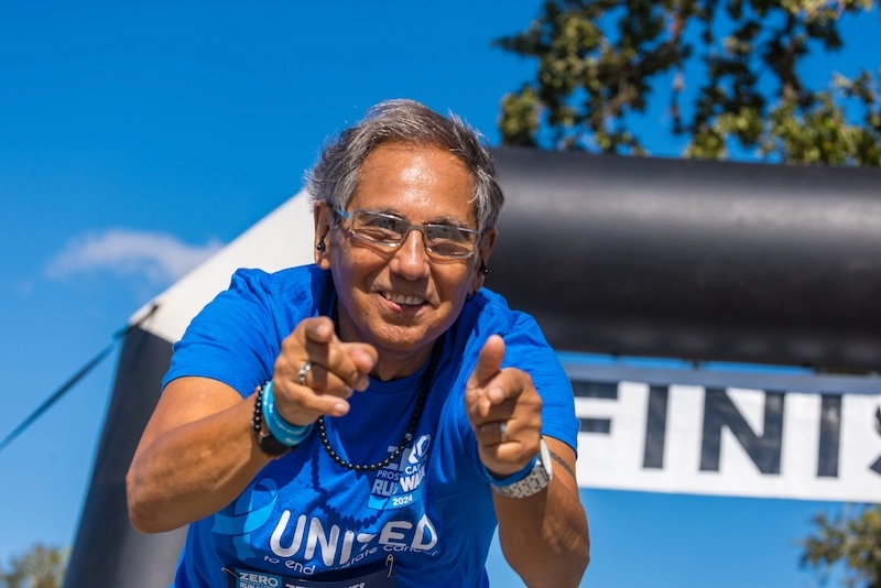 A male race participant leans down and enthusiastically points at the camera with both hands at the finish line. A male race participant leans down and enthusiastically points at the camera with both hands at the finish line.