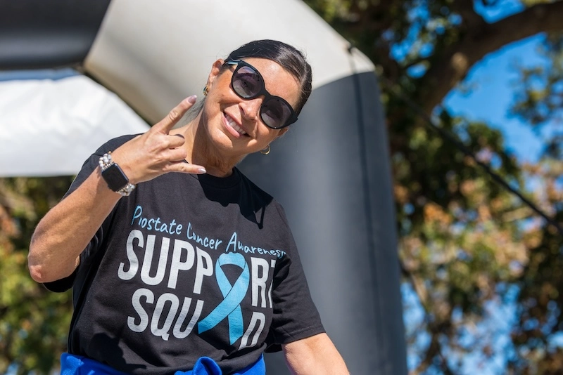 A female race participant smiles at the camera wearing a shirt that says, ‘Prostate Cancer Awareness Support Squad’.