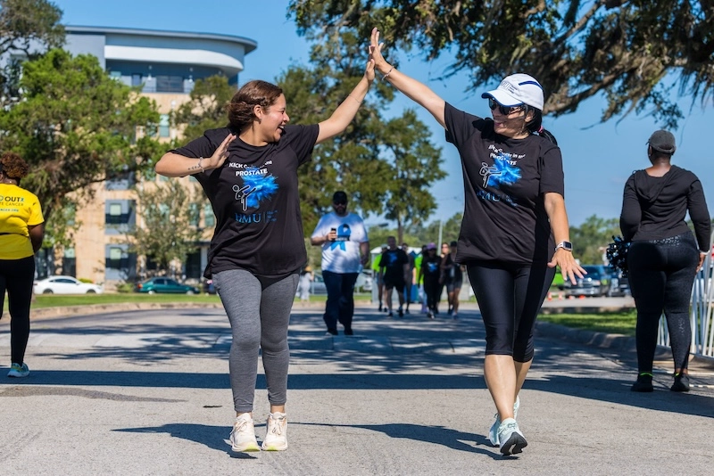 Two female race participants high five each other during the race with other participants in the background. Two female race participants high five each other during the race with other participants in the background.