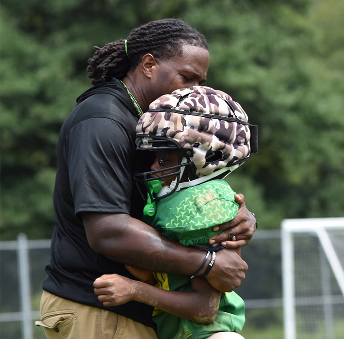 Featured: Coach Kiven with a young member of the Montgomery Village Chief athletes. The full time volunteer job requires coaching, mentoring, educating and emotional support.